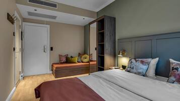 A bedroom with a large bed, a bench with cushions, a wardrobe, and a door.