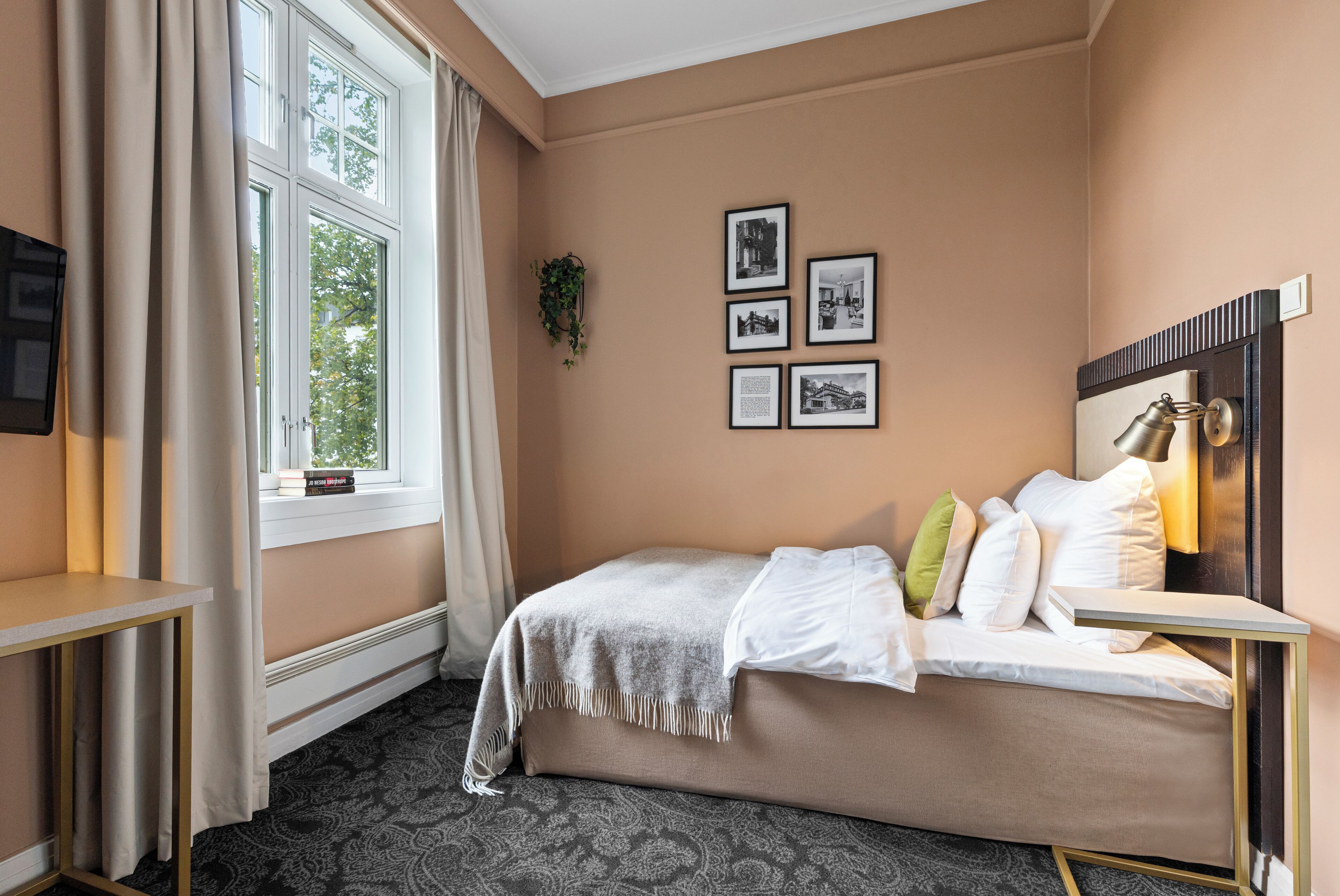 Ein Schlafzimmer mit Bett, Nachttisch, einem Fenster mit Vorhängen und gerahmten Bildern an der Wand.