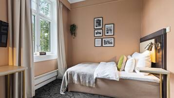 Ein Schlafzimmer mit Bett, Nachttisch, einem Fenster mit Vorhängen und gerahmten Bildern an der Wand.