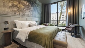 A modern hotel room with a large bed, a seating area, a view of the city, and a unique wall mural. - Home Hotel Gabelshus (Oslo)