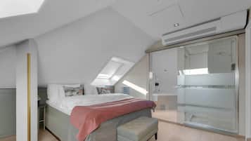 A modern bedroom with a large bed, a bench, a walk-in closet, and a skylight.