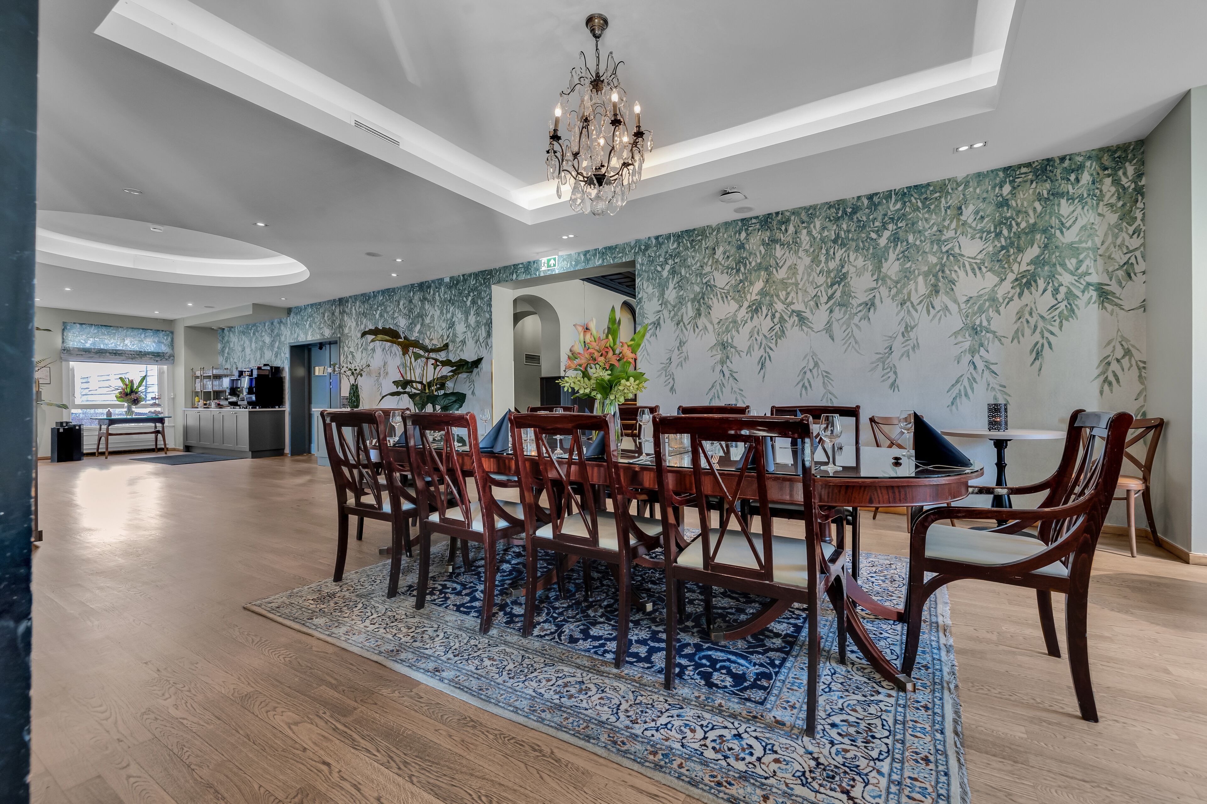 A spacious dining area with a large wooden table and chairs, a chandelier, and a patterned wall.