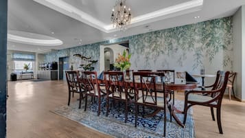 A spacious dining area with a large wooden table and chairs, a chandelier, and a patterned wall.