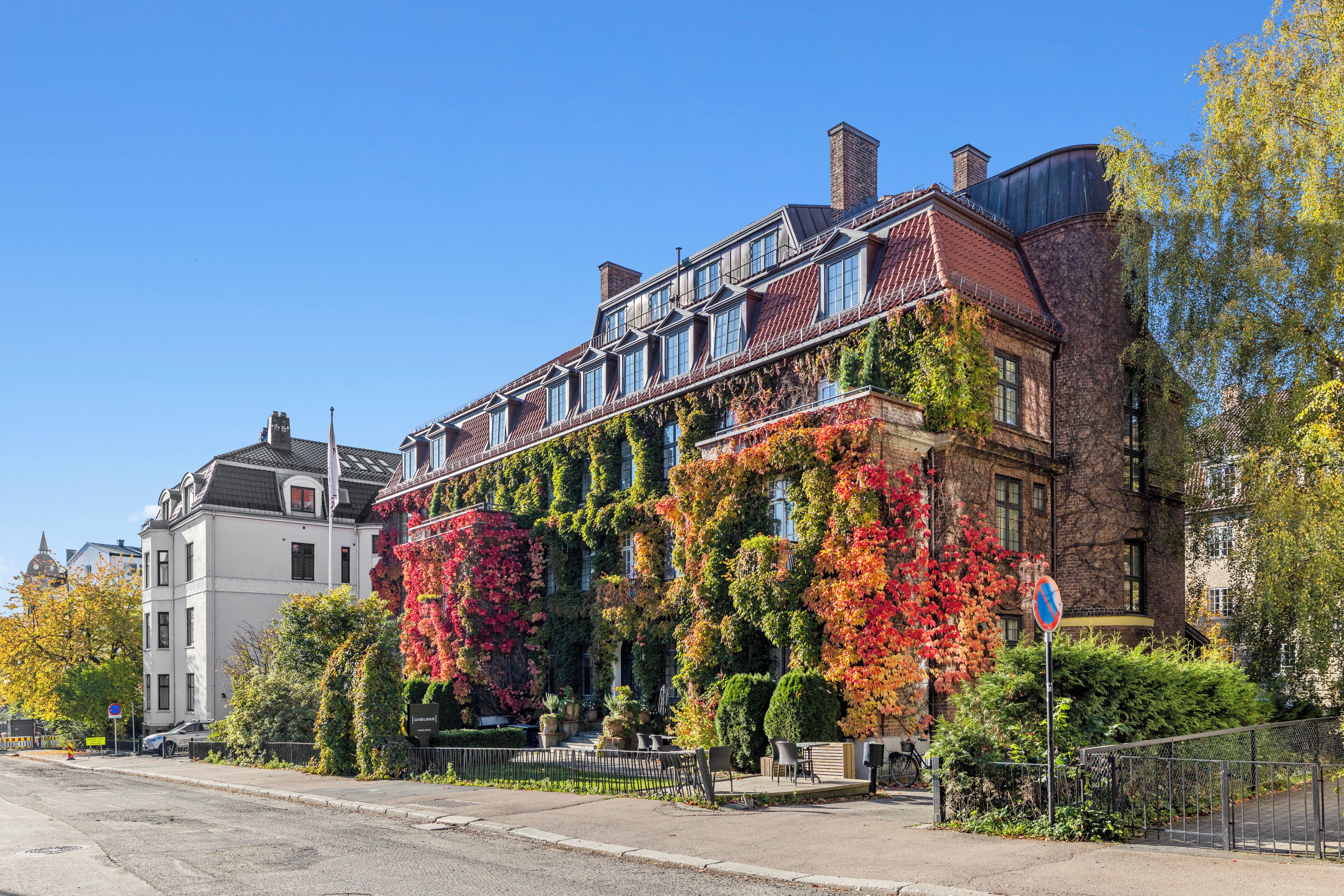 A historic building with a brick facade, large windows, and a balcony with climbing plants.