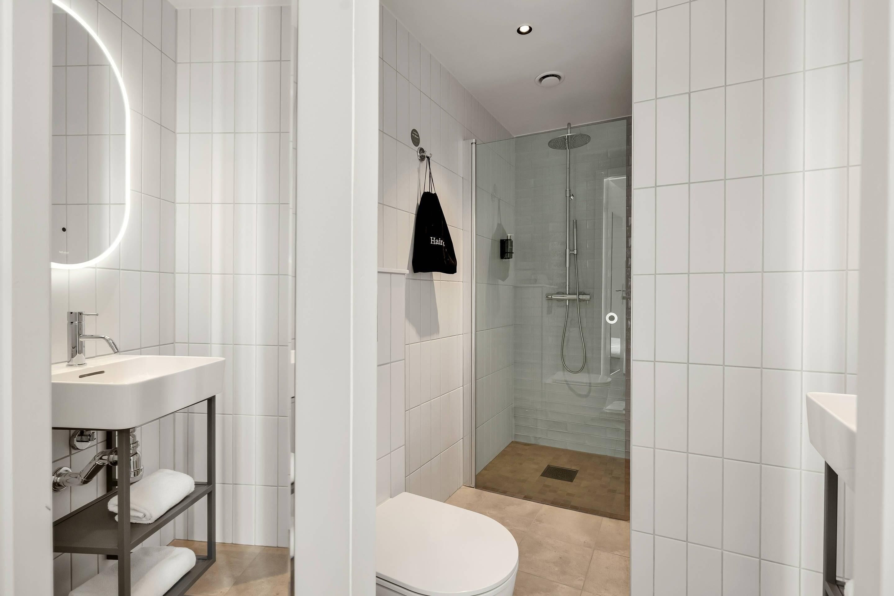 Ein modernes Badezimmer mit einem weißen Waschbecken, einer Toilette, einer Duschkabine und einem Handtuchhalter mit einer schwarzen Tasche.