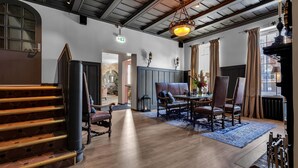 A spacious room with a wooden staircase, a dining area with a table and chairs, and a large window with curtains. - Home Hotel Gabelshus (Oslo)