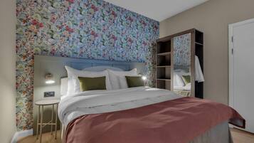 Un dormitorio con papel tapiz floral, una cama con ropa de cama blanca, una mesita de noche y un armario con espejo.