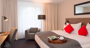 Habitación de hotel con cama, escritorio, silla, lámpara y ventana con cortinas.