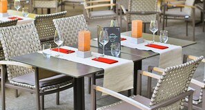 Un ambiente de restaurante con mesas dispuestas para comer, destacando sillas tejidas y una vajilla impecable.