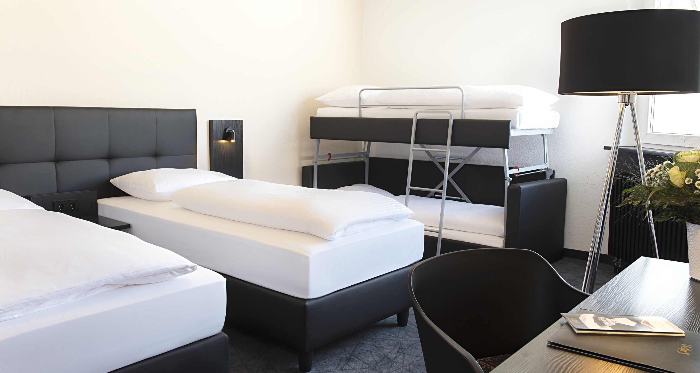 A hotel room with two beds, a desk, a chair, a lamp, and a potted plant.