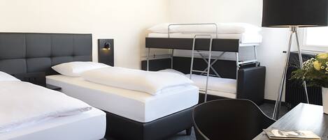 A hotel room with two beds, a desk, a chair, a lamp, and a potted plant.