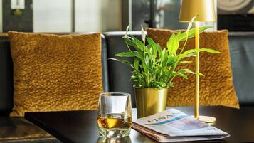 A table with a glass of whiskey, a plant in a gold pot, and a newspaper.