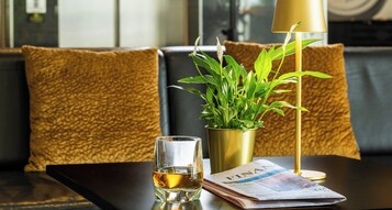 A table with a glass of whiskey, a plant in a gold pot, and a newspaper.