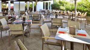 Un espacio de comedor al aire libre con sillas y mesas de mimbre, algunas con menús y vasos.