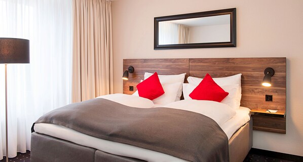 Una cama bien tendida con un cabecero de madera, dos mesitas de noche con lámparas y un espejo grande sobre la cama.