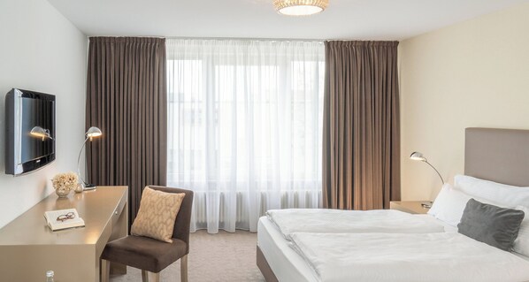 A hotel room with a bed, a desk, a chair, a TV, and a window with curtains.