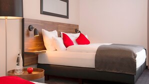 Habitación de hotel con una cama, una mesita de noche con una botella y vasos, una manzana roja y una lámpara.
