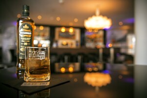 Un bar con una botella de whisky y un vaso sobre un tapete.