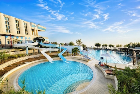 A swimming pool with a water slide, lounge chairs, and a building with a modern design.. Oryx Grand Jebel Hafeet