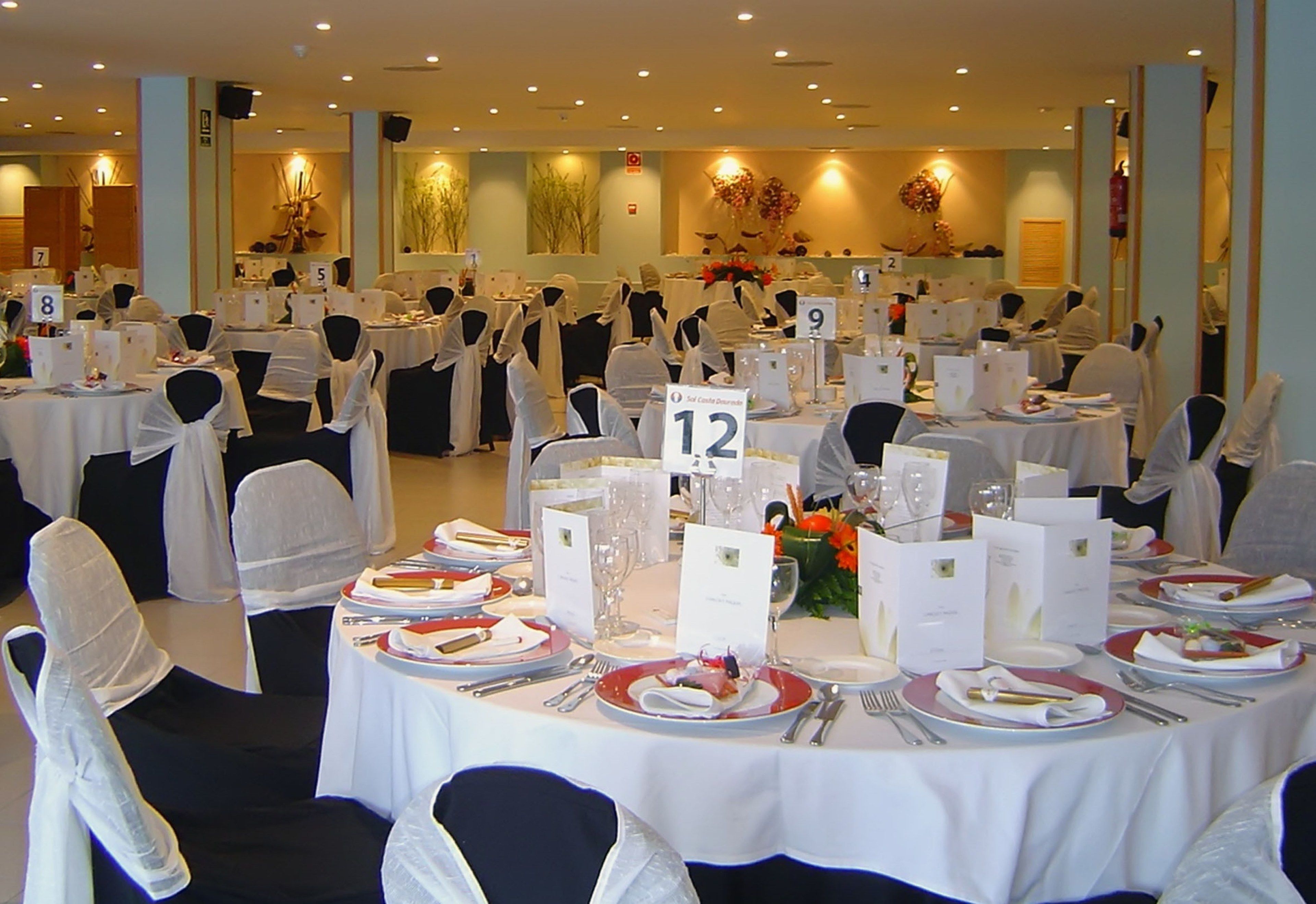 A banquet hall with round tables numbered 5 to 12, white tablecloths, and black chairs with white sashes.