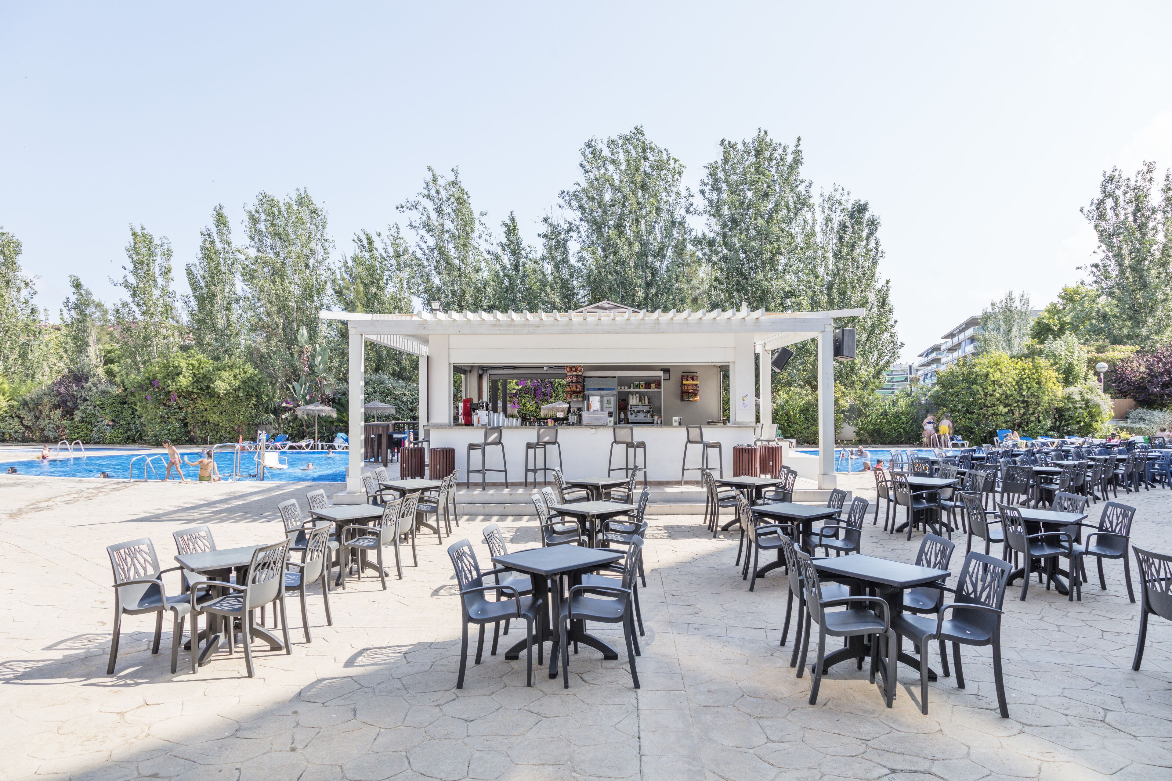 An outdoor patio area with tables and chairs, a pool, and a bar area.