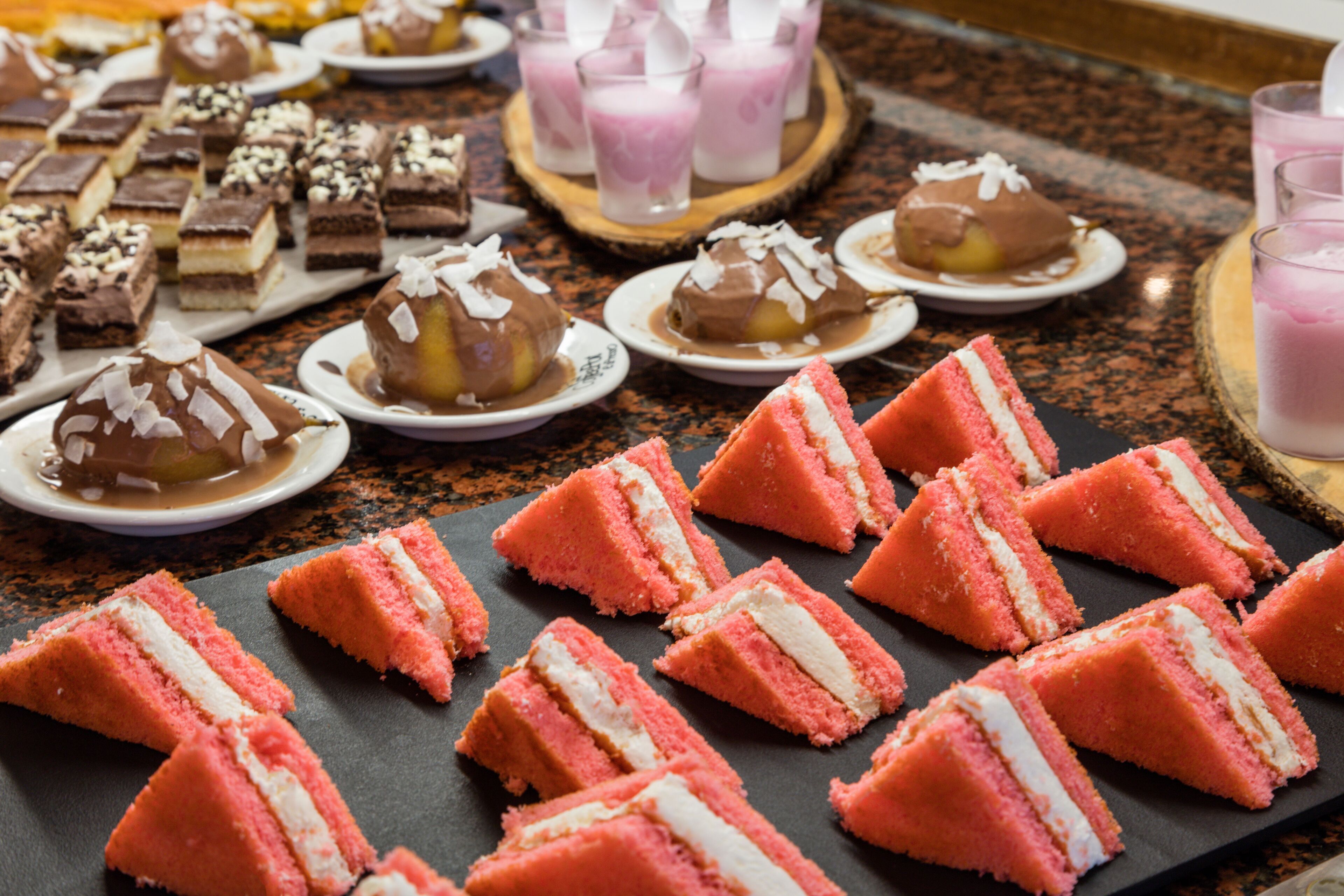 Variedad de postres en una mesa buffet, incluyendo pasteles rosados en capas y postres de chocolate con cobertura.