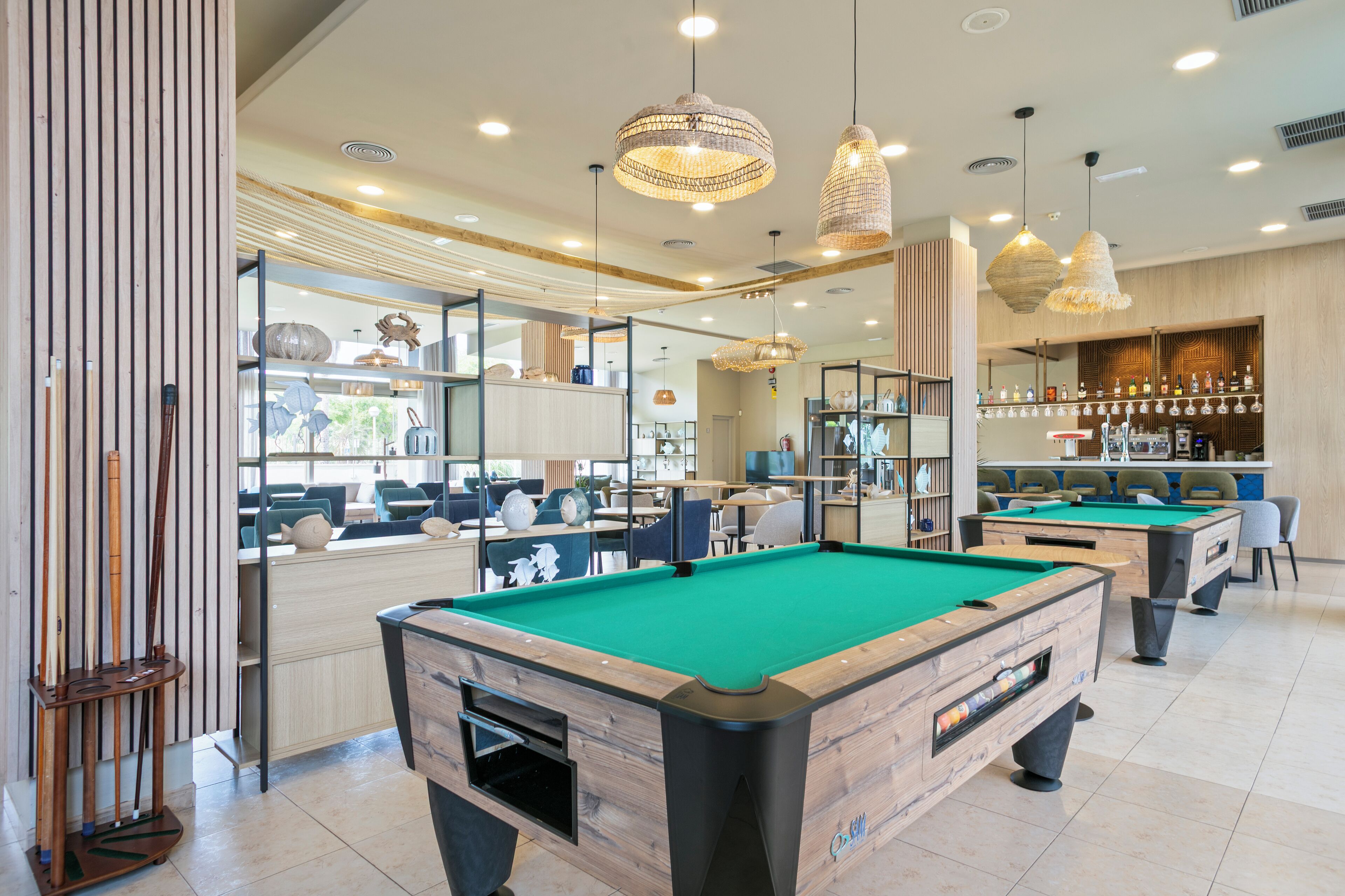 A pool hall with multiple pool tables, wooden accents, and hanging pendant lights.