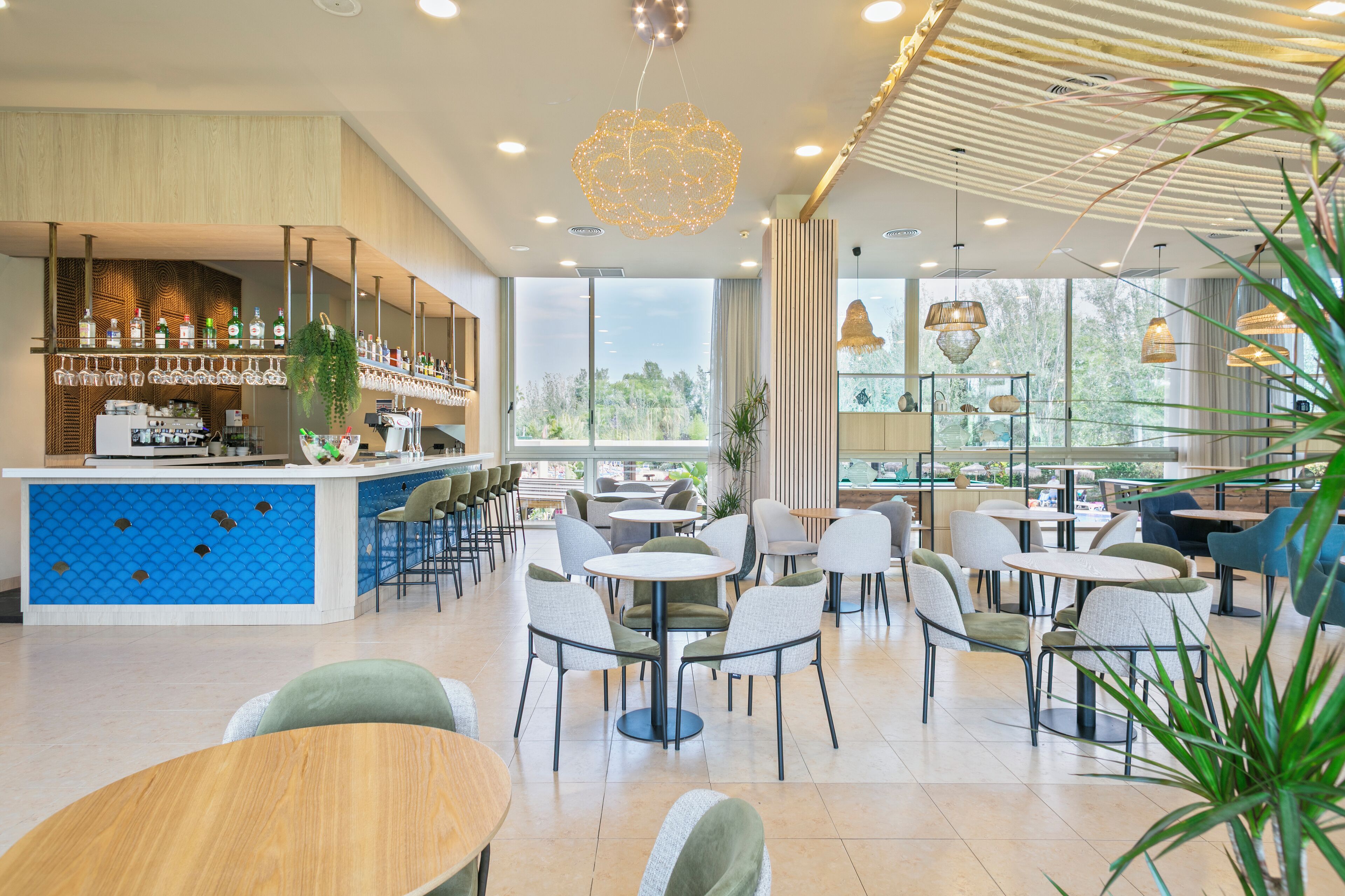A modern cafe with a bar area, multiple seating options, and large windows offering a view of the outdoors.