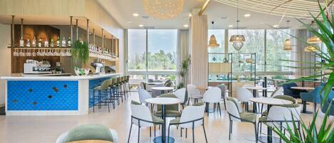 Una cafetería moderna con barra, varias opciones de asientos y grandes ventanales con vistas al exterior.