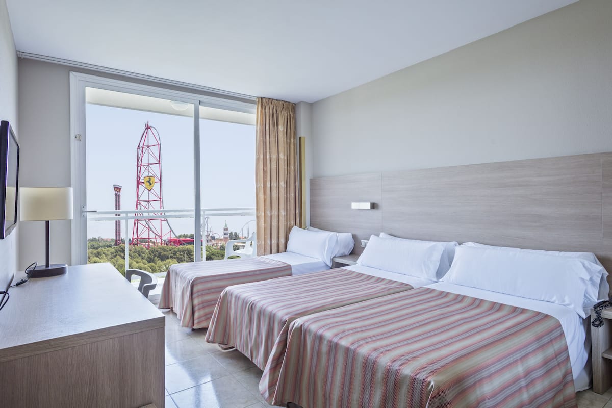 A hotel room with two beds, a desk, and a large window offering a view of a red tower.