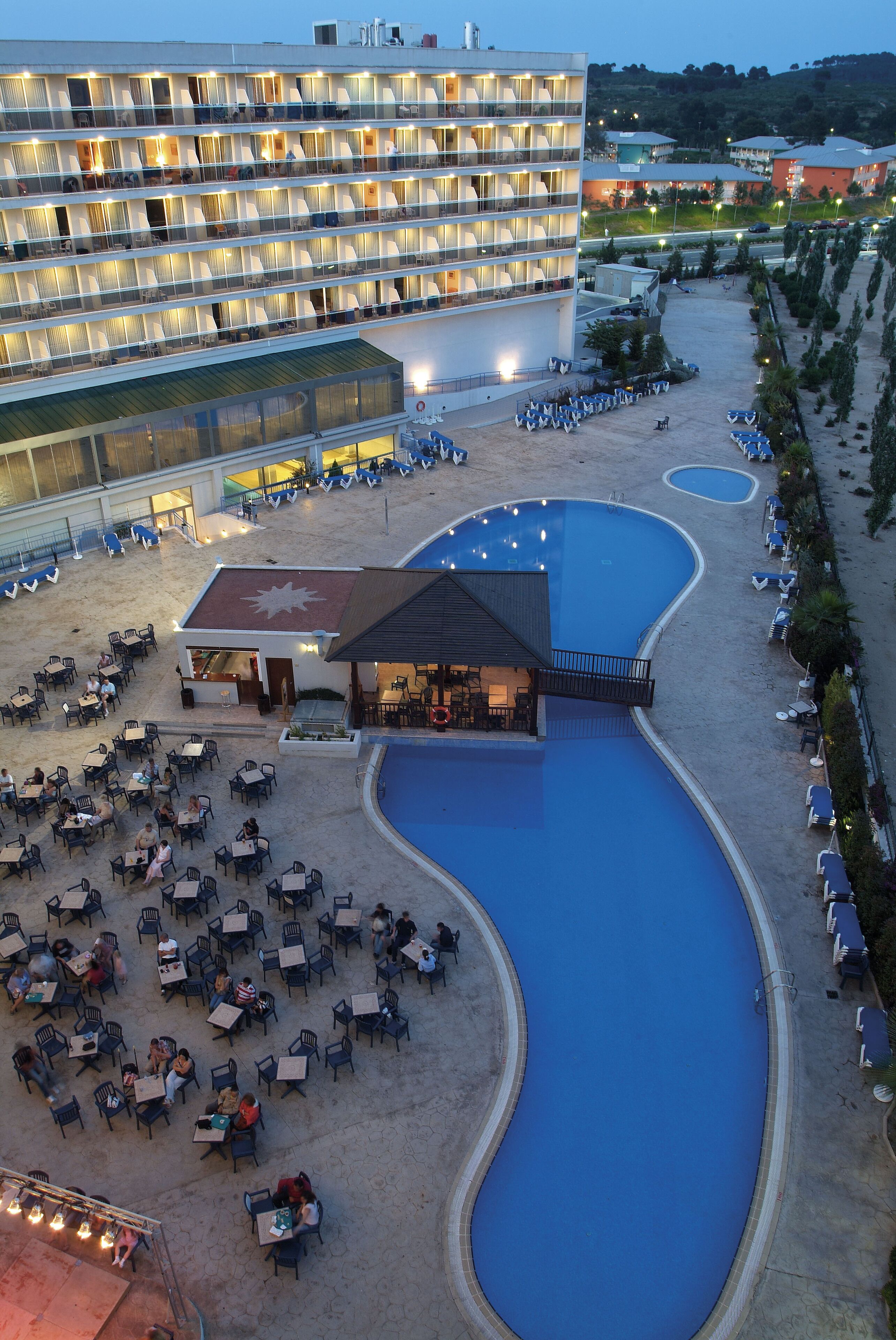 A hotel with multiple floors, outdoor pool, and dining area with tables and chairs.
