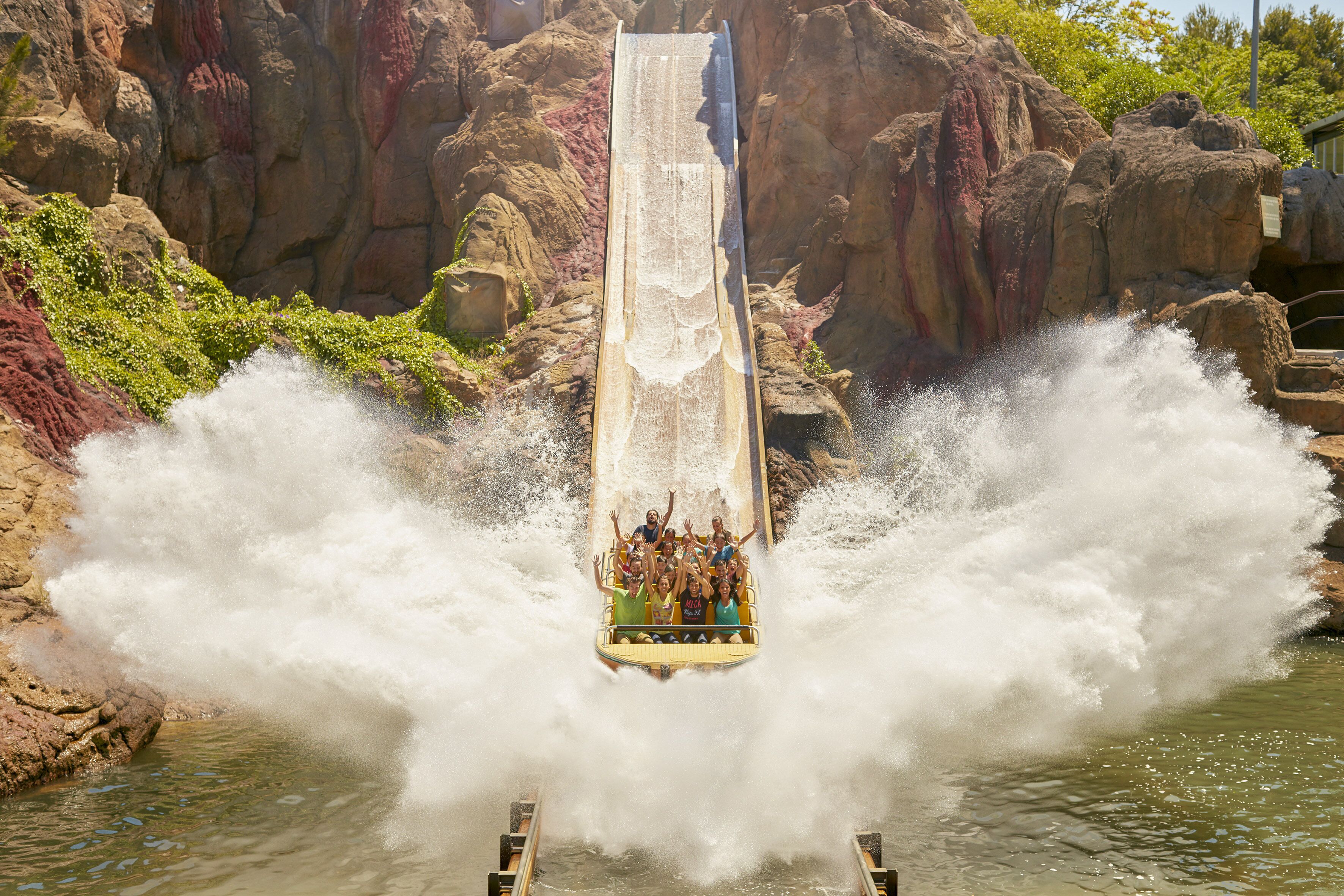 Un toboggan aquatique avec des personnes en haut, entouré d’un paysage rocheux.
