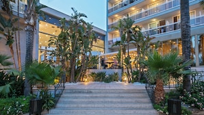 A multi-story hotel with outdoor seating areas, palm trees, and a staircase leading to the entrance. - Sol Costa Daurada (Salou)