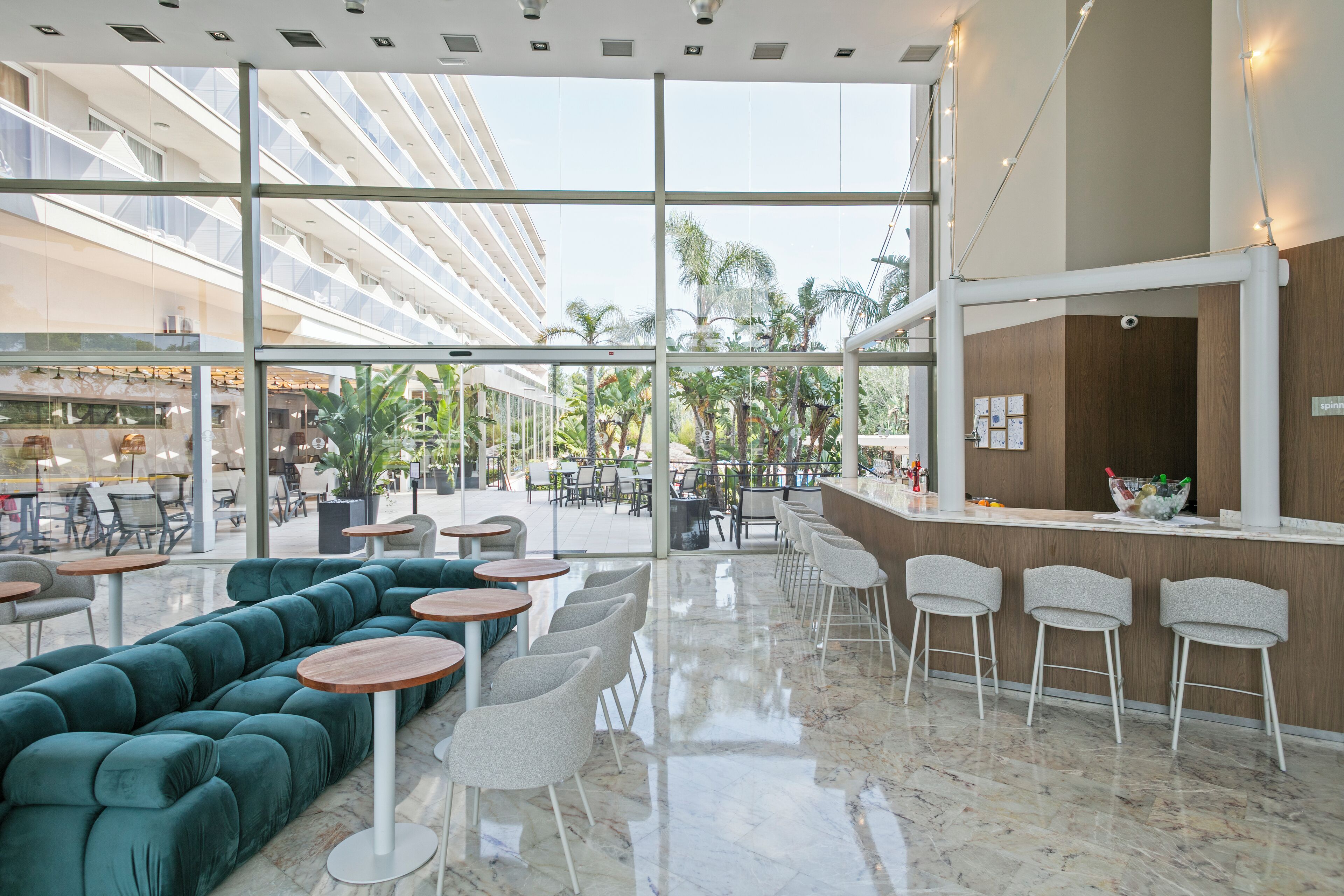 Un moderno vestíbulo de hotel con un sofá verde, mesas redondas y una zona de bar.