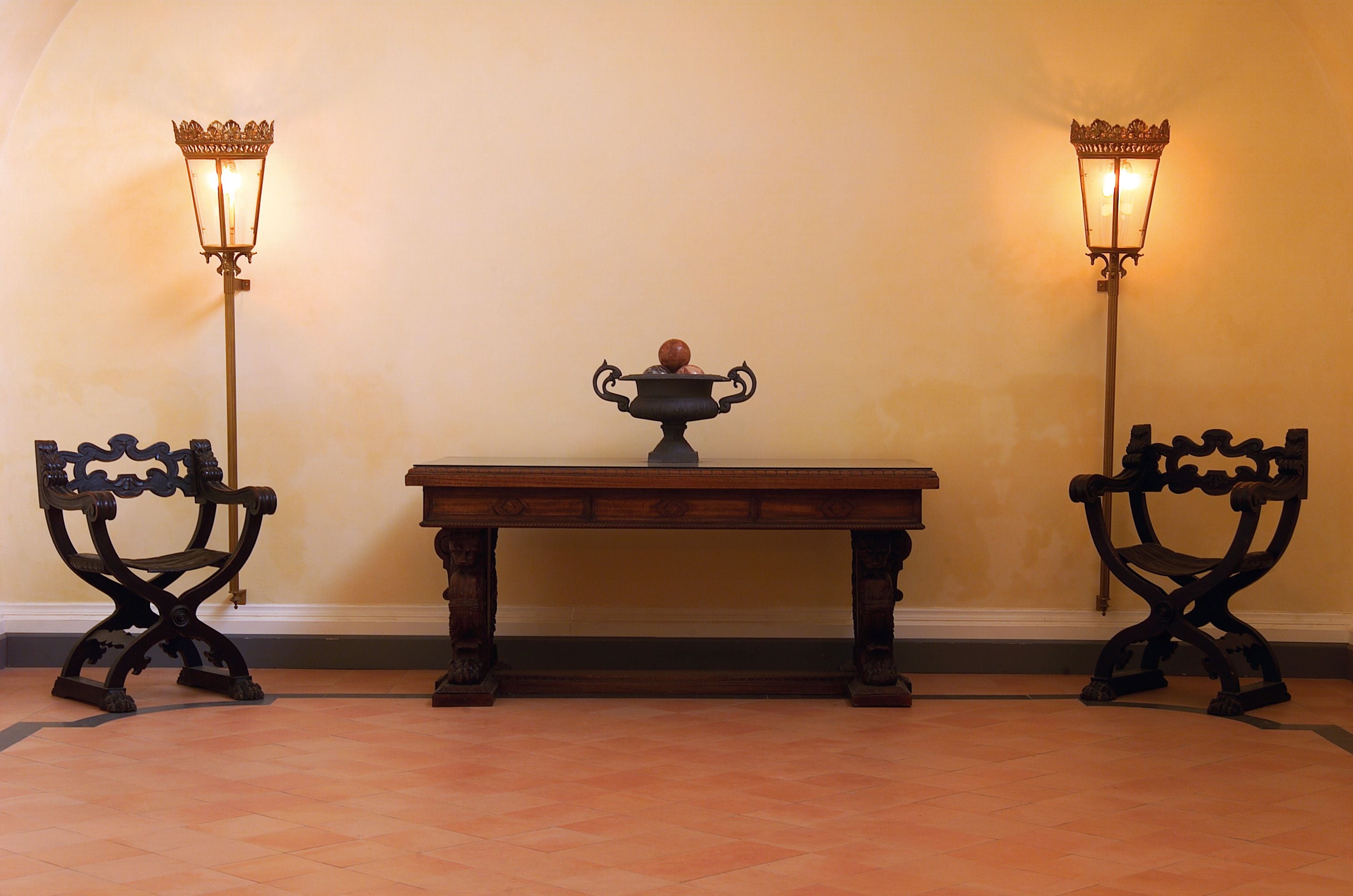 A room with a wooden table and two ornate chairs, each with a wall-mounted light fixture.