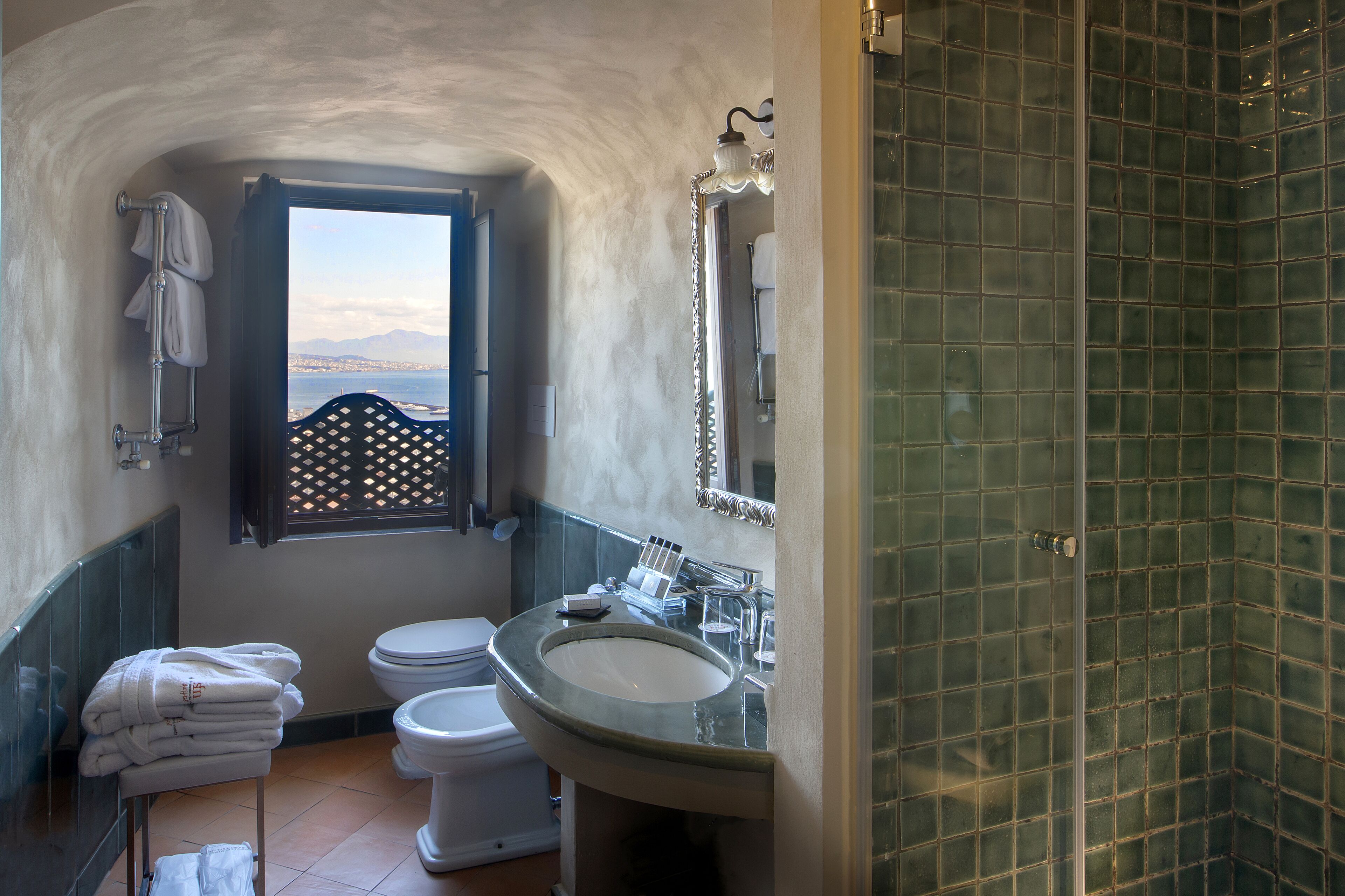 A bathroom with a view of the sea, a sink, a toilet, and a shower area.