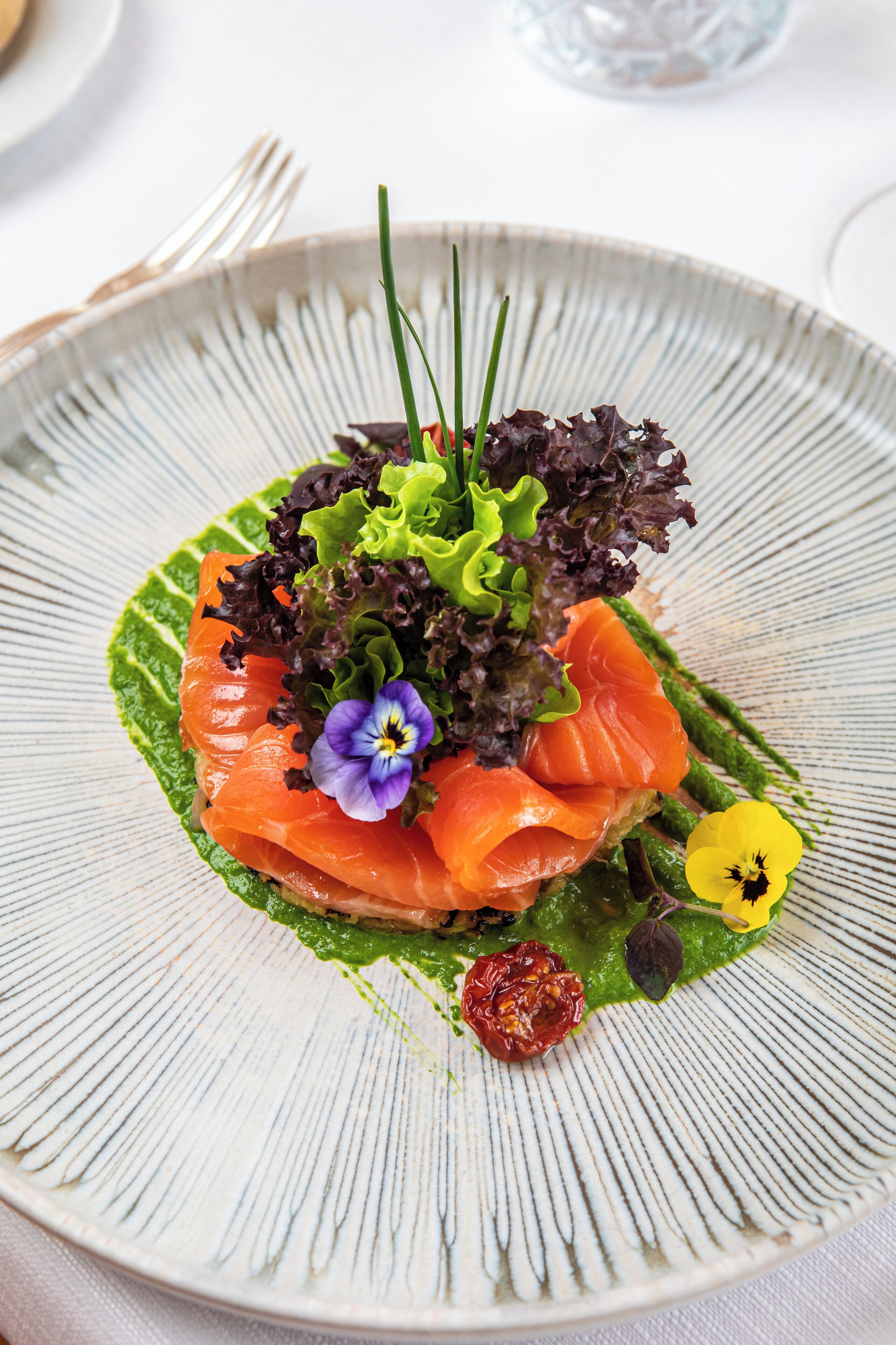 A plate with a dish of smoked salmon, greens, and flowers.