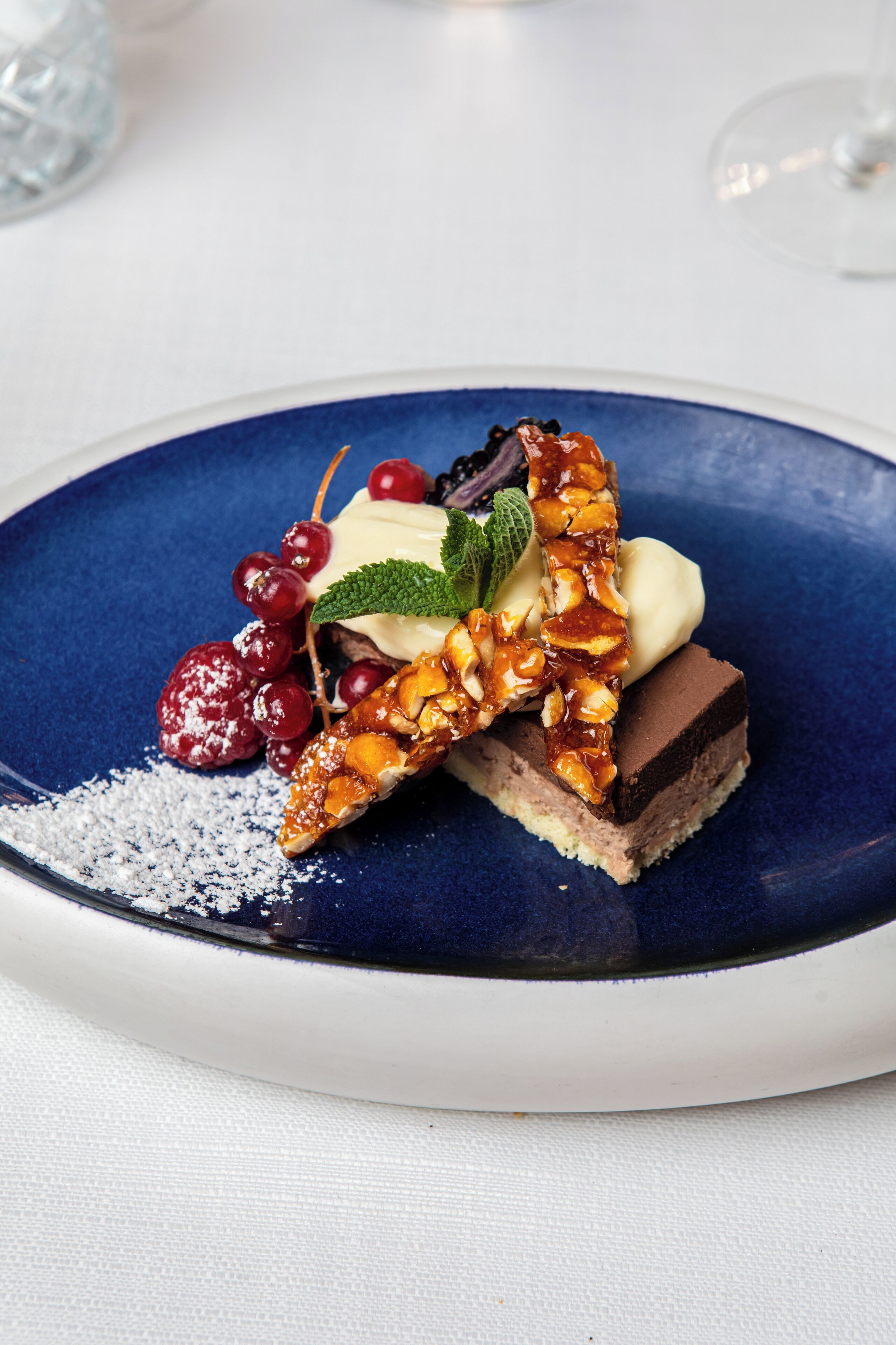 A dessert on a blue plate with cherries, mint, and a chocolate layer.
