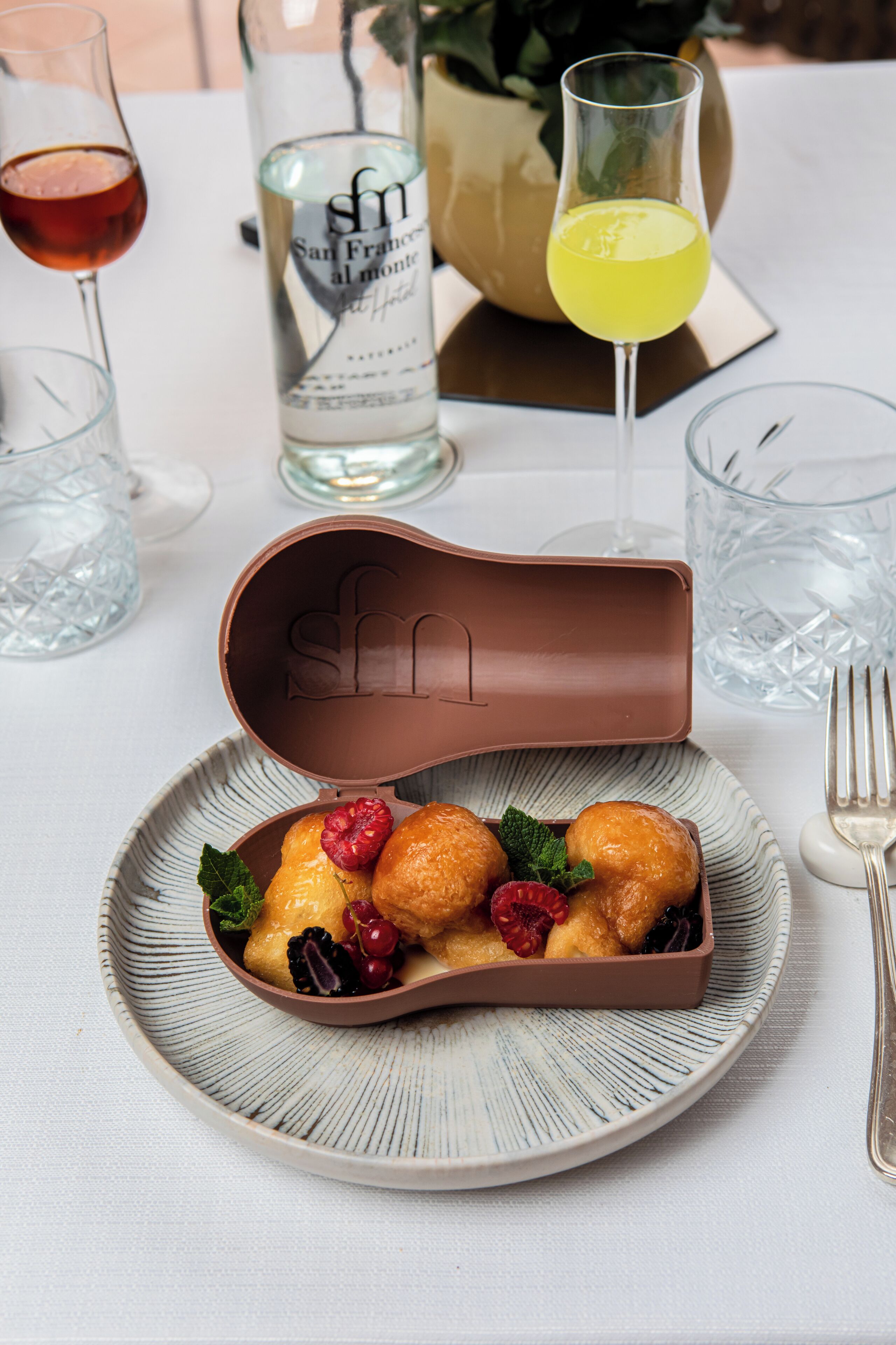 A dessert plate with pastries and berries, a bottle of wine, and glasses on a table.