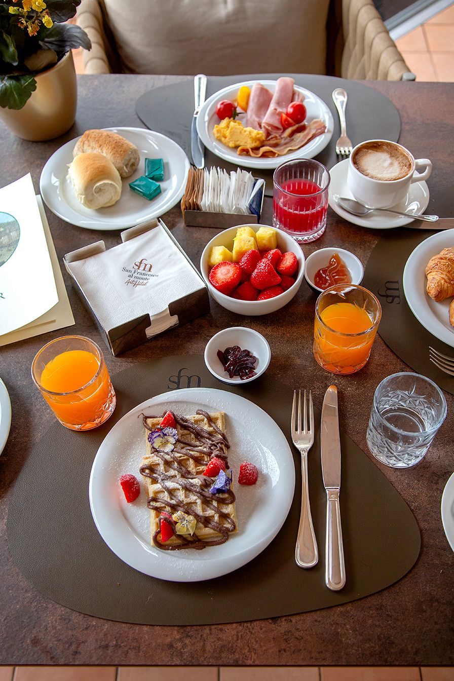 A breakfast table with plates of food, a coffee cup, and a fruit bowl.