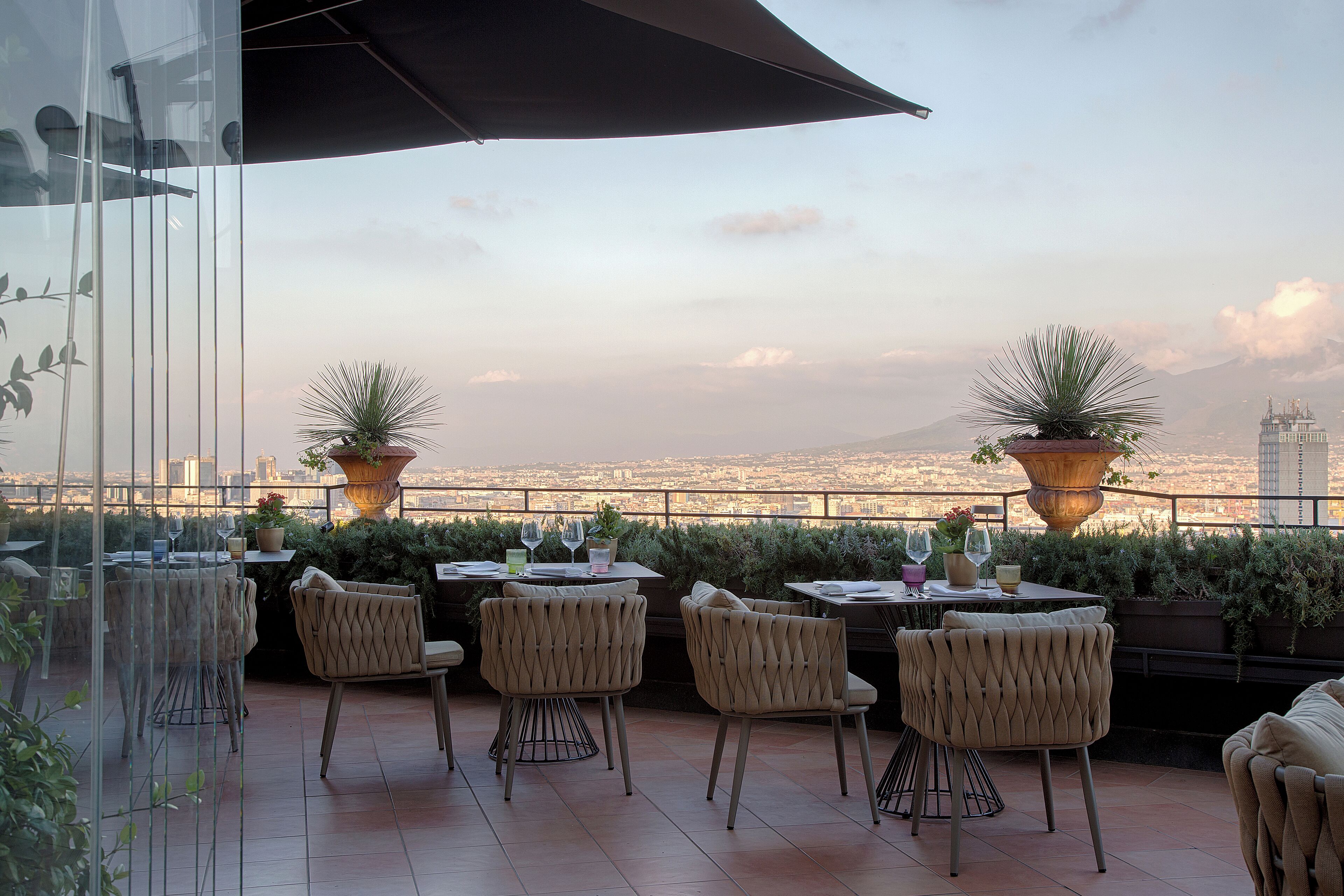 Una terrazza all'aperto con tavoli e sedie, piante in vaso e vista sulla città.