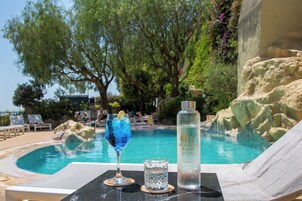 A poolside setting with a drink, a bottle, and lounge chairs.