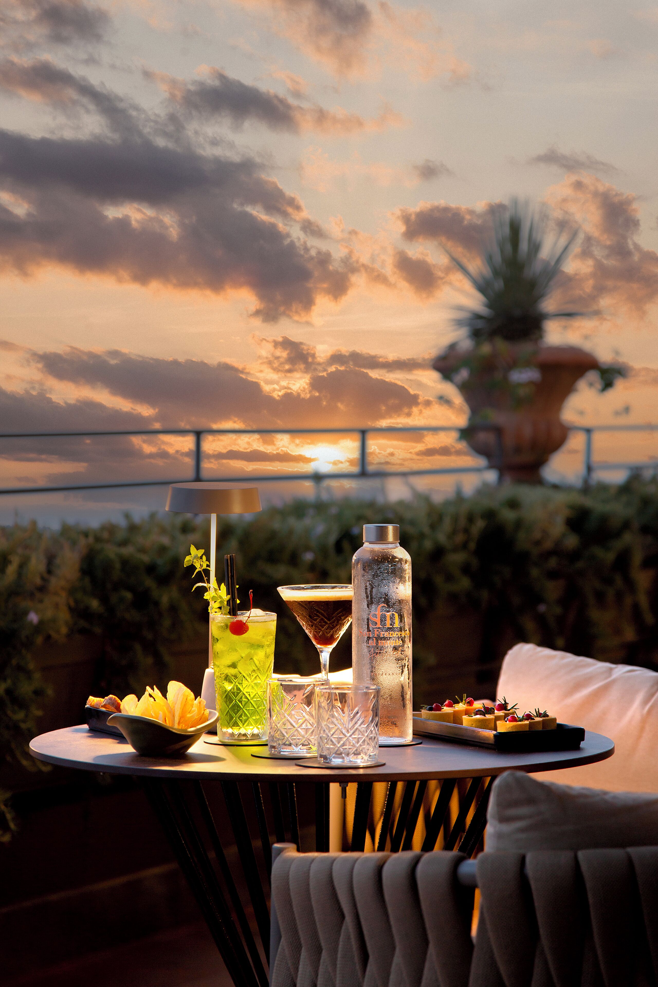 Une table dressée avec des boissons et des amuse-gueules, offrant une vue sur le coucher du soleil.