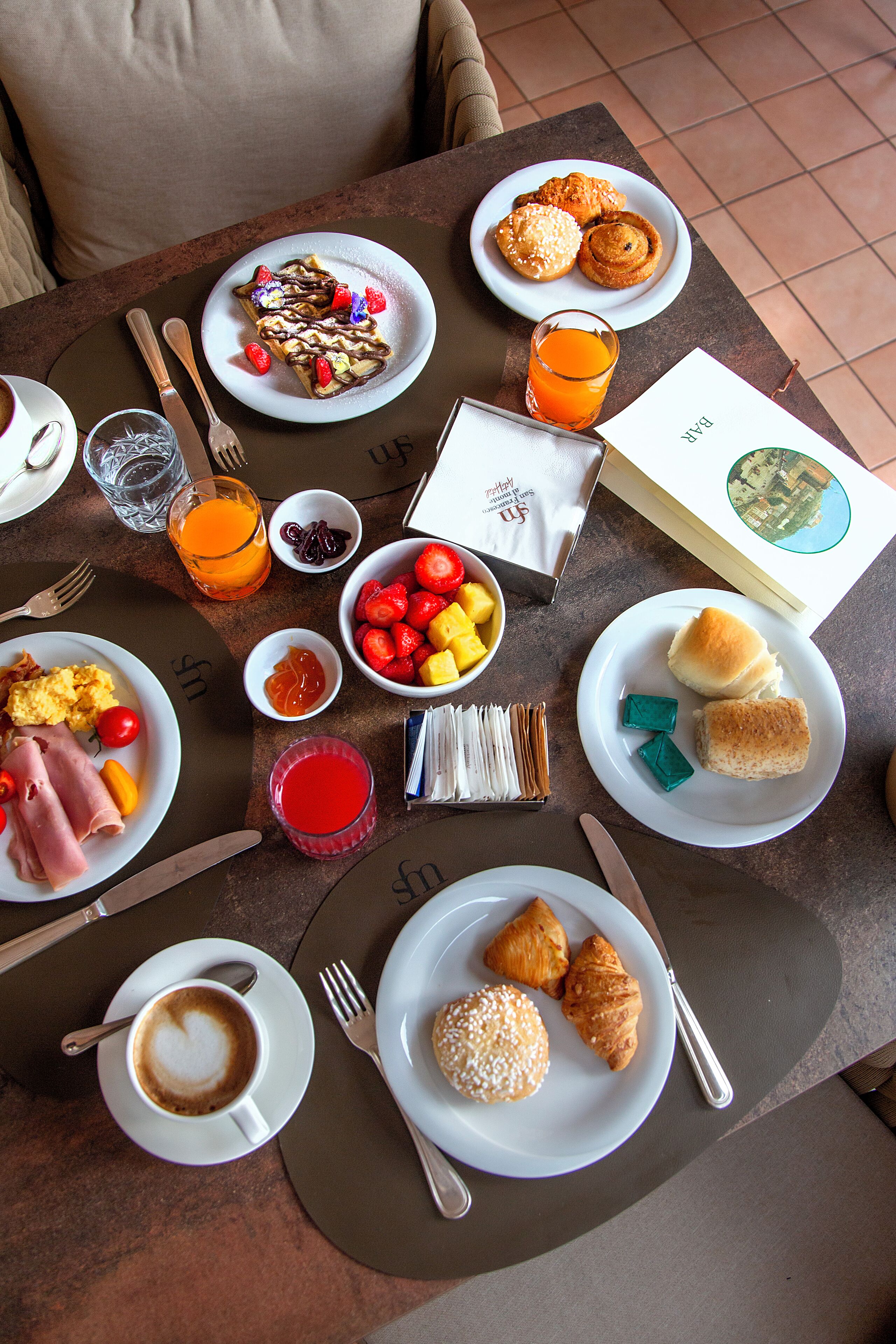 Une table de petit-déjeuner avec des assiettes remplies de nourriture, un verre de jus d’orange et un menu.