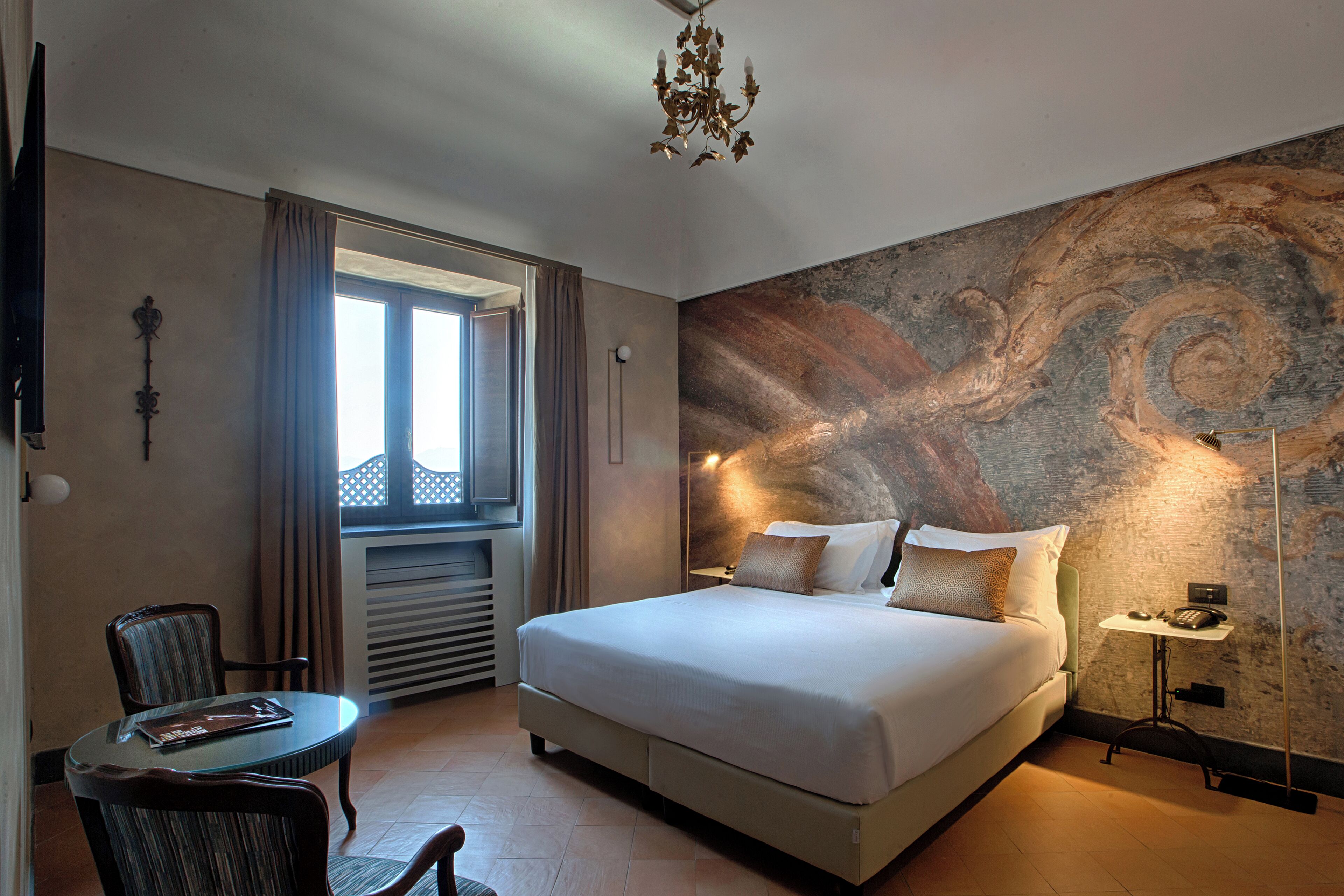 A modern hotel room with a large bed, a dining table, and a view of the outdoors.