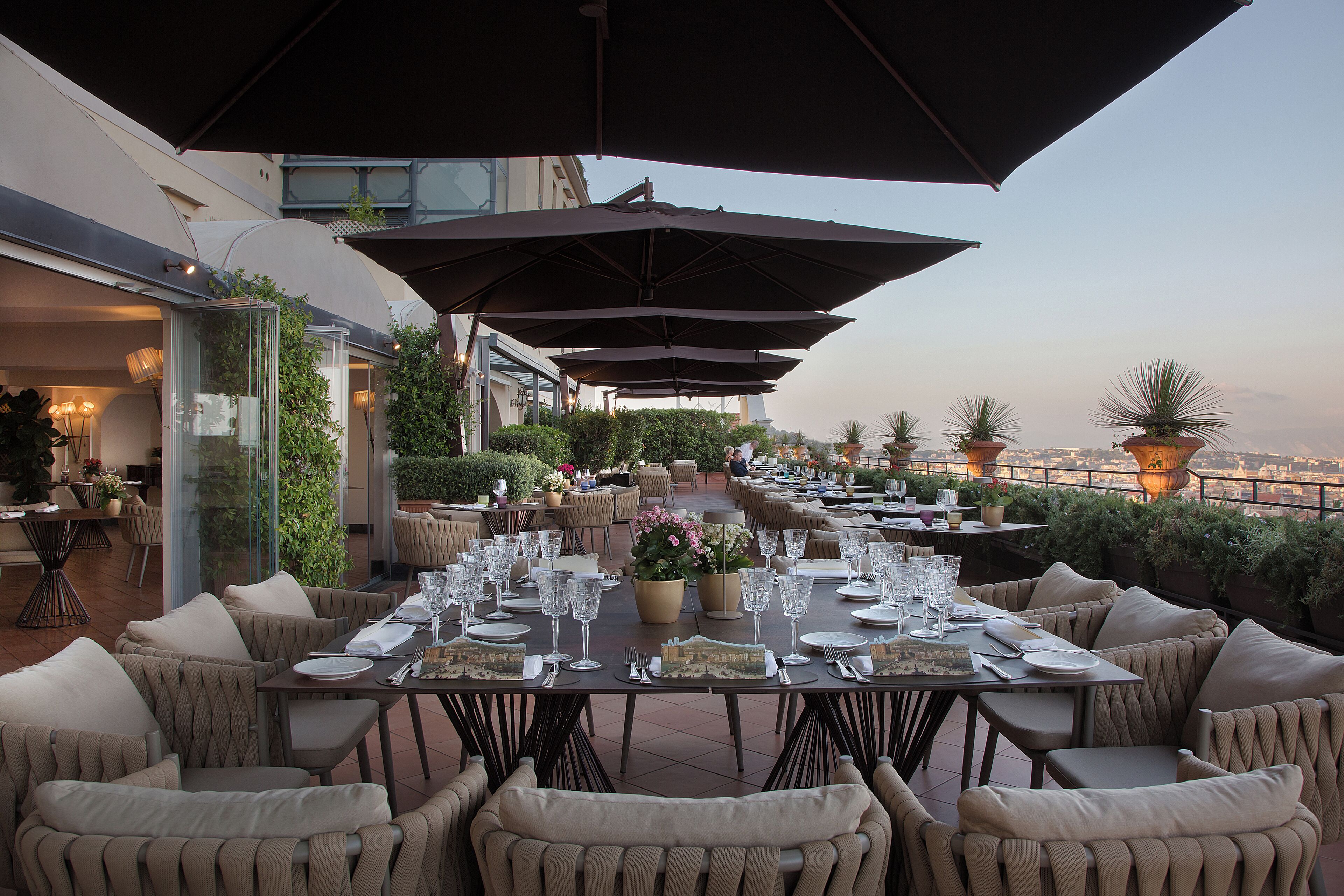 An outdoor dining area with tables set for a meal, surrounded by large umbrellas and comfortable seating.