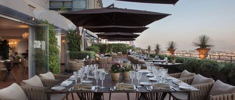 An outdoor dining area with tables set for a meal, surrounded by large umbrellas and comfortable seating.
