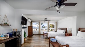 A hotel room with two beds, a TV, a ceiling fan, and a view of the ocean through large windows. - Casa Isleña Inn (Rincon)