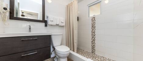A bathroom with a white toilet, dark wooden vanity, a large mirror, and a shower area with a tiled floor.