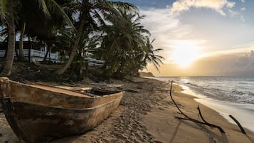Una playa con un barco grande, palmeras y un atardecer.